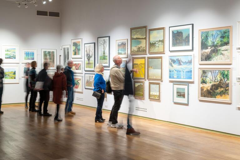 a group of exhibition visitors observe a wall of pastel artworks