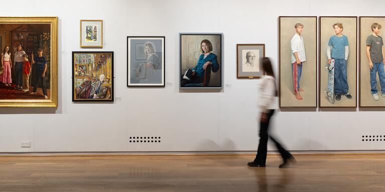 A visitor walks through the gallery, passing a series of portrait paintings