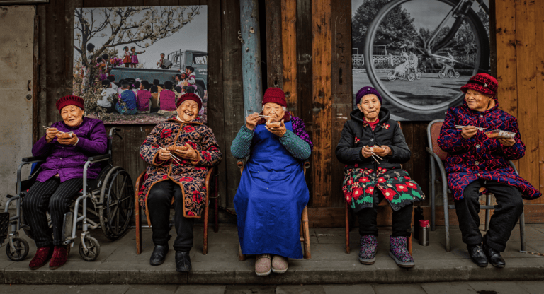 5 elderly women sat on chairs eating food
