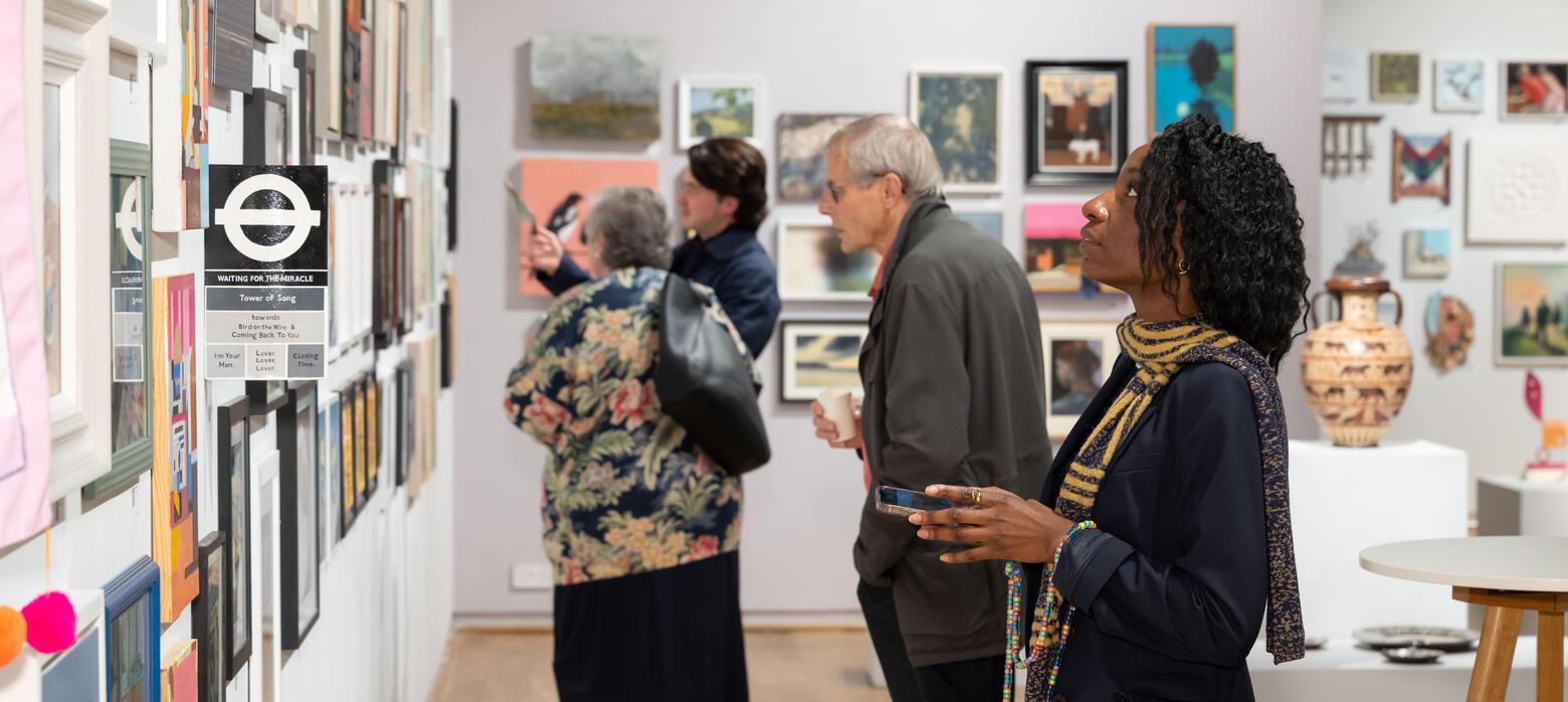 Lady looks at work on wall with figures behind her