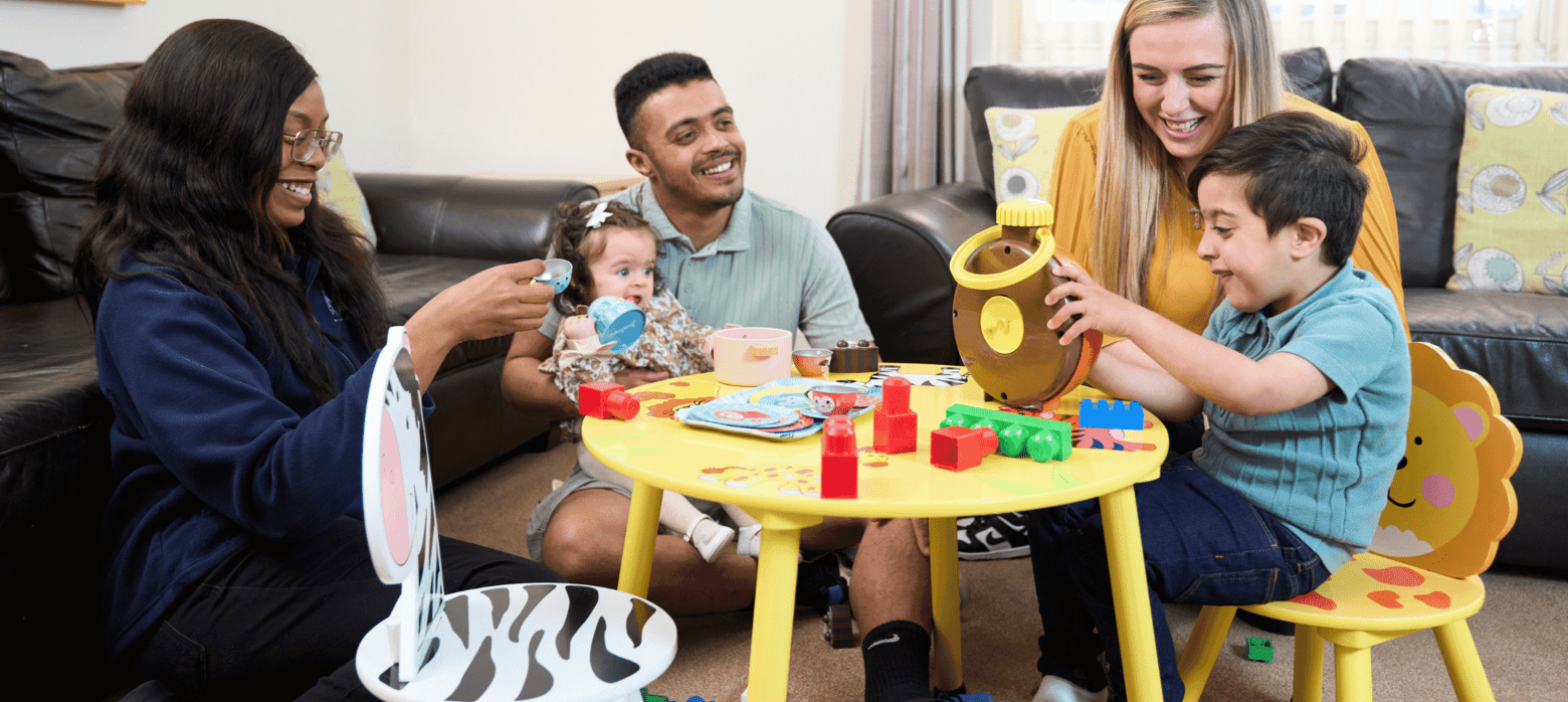 three adults and two children sat playing around a small table