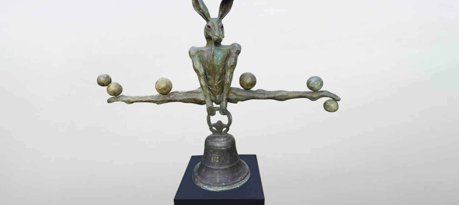 a metal sculpture of a rabbit doing the splits over a bell