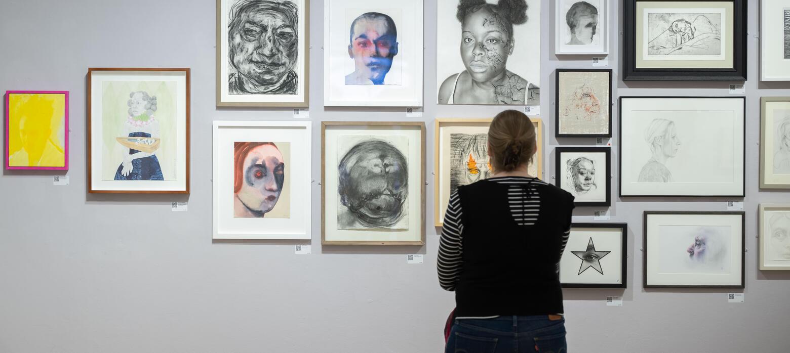 Person looks at wall of portraits with back to camera