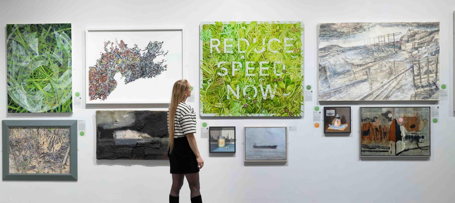 Woman in heeled boots looks at 'Reduce Speed Now' painting