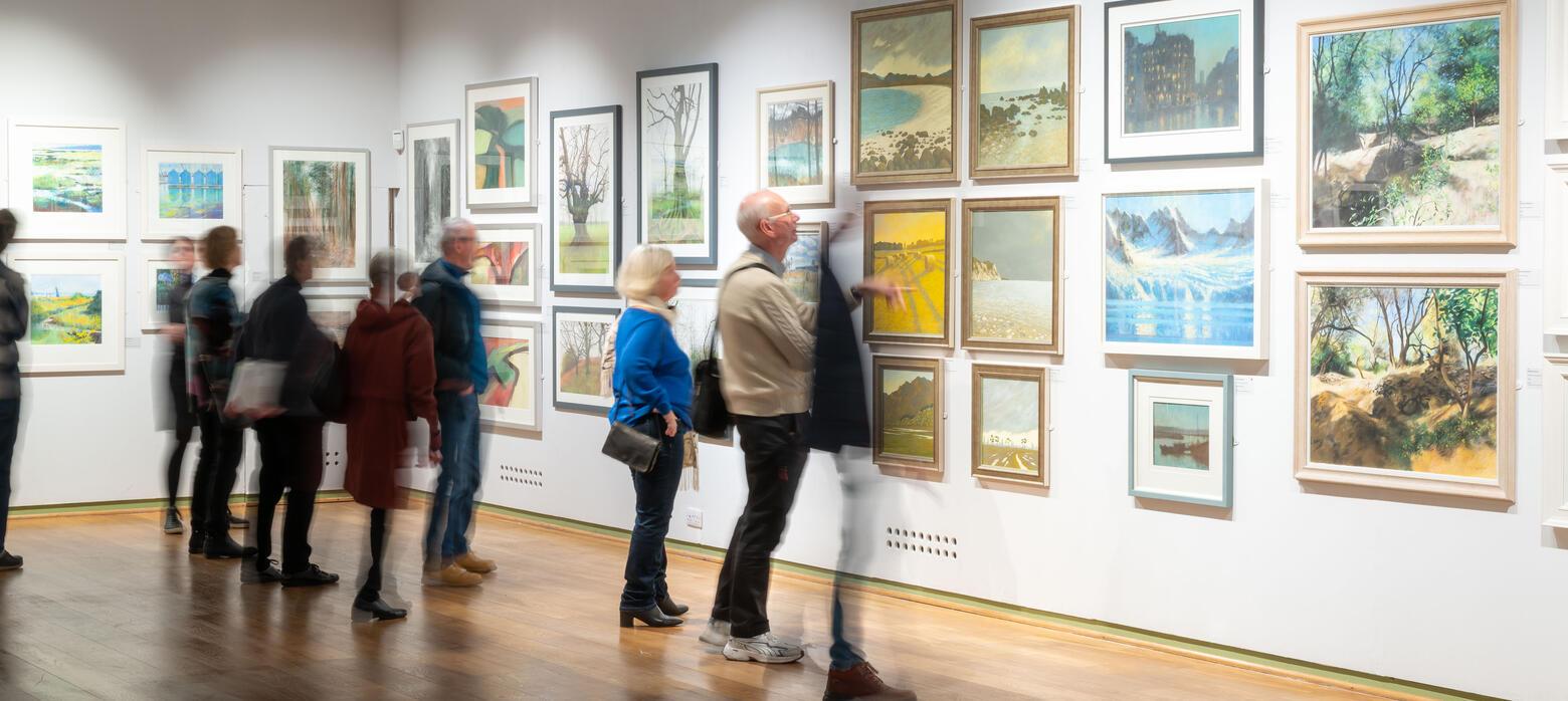 a group of exhibition visitors observe a wall of pastel artworks