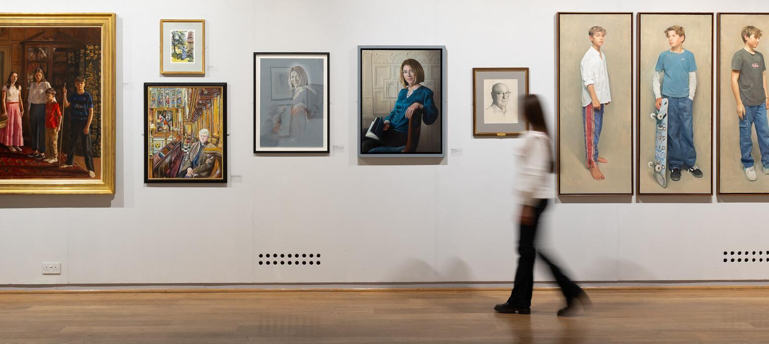 A visitor walks through the gallery, passing a series of portrait paintings