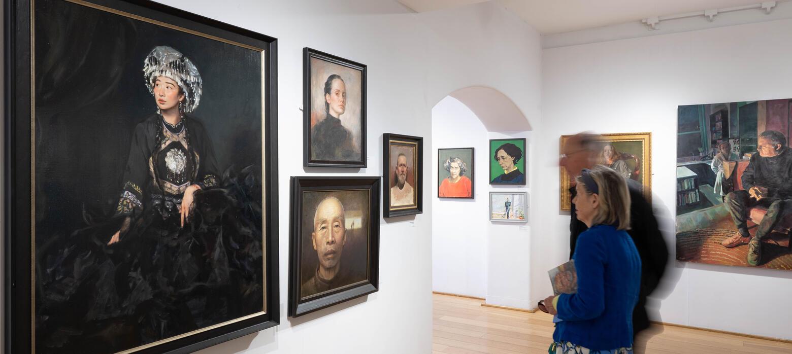 Two figures look at large portrait of lady in dark colours