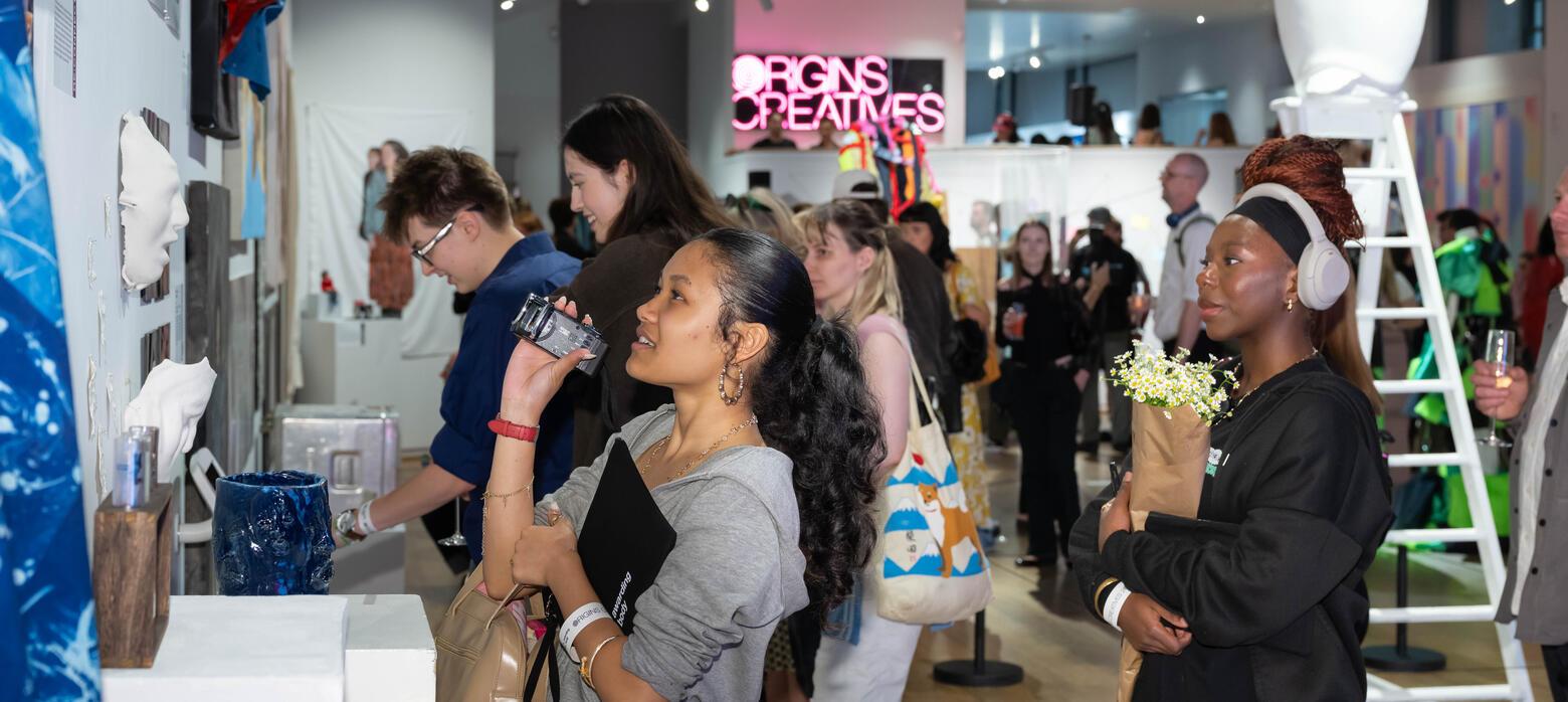 Group of people look at work on wall with bright pink neon sign behind