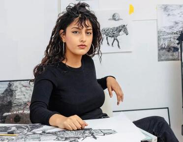 Artist Rizza Zahid seated in front of sketches