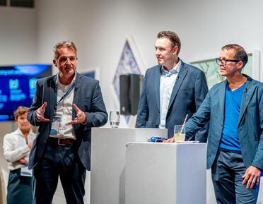 3 men standing in front of plinths in the west gallery giving a presentation