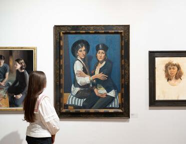 A visitor observes a wall of portrait paintings.