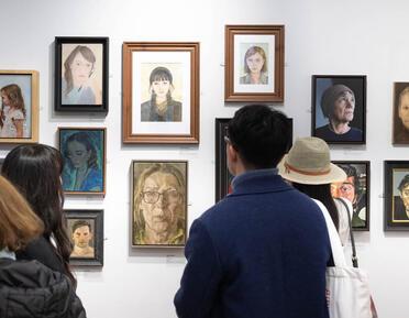 A man looking at a wall of portrait paintings