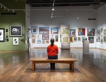 young woman sitting on a bench at Mall Galleries looking at paintings on the wall 