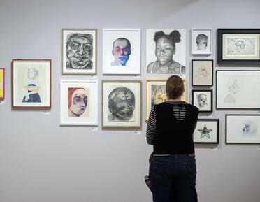 Person looks at wall of portraits with back to camera