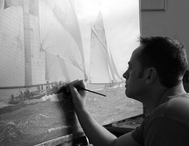 Black and White photograph of Jamie Medlin working on large yacht painting in studio