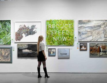 Woman in heeled boots looks at 'Reduce Speed Now' painting