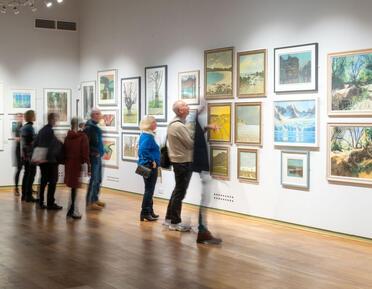 a group of exhibition visitors observe a wall of pastel artworks