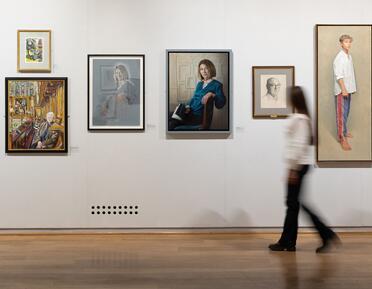 A visitor walks through the gallery, passing a series of portrait paintings