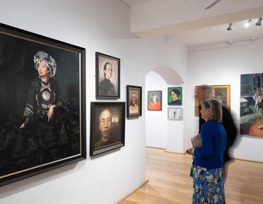 Two figures look at large portrait of lady in dark colours